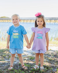 Two children holding hands outdoors, wearing matching outfits with fish designs.